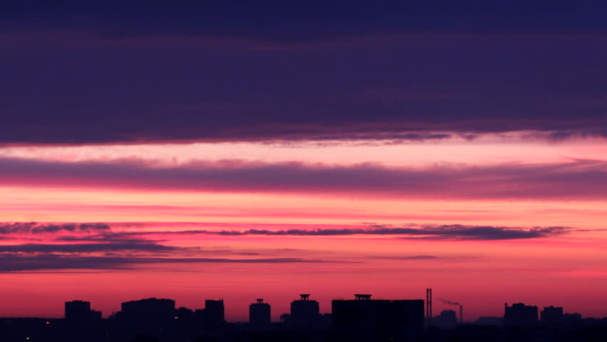 Fast moving in different directions, low clouds over the silhouette city. Change the color of sunrise