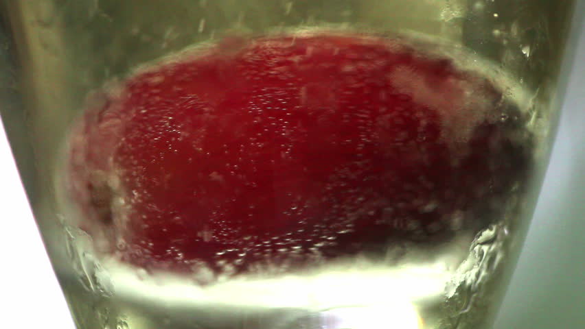 Red grapes falling into glass of golden bubbling champagne