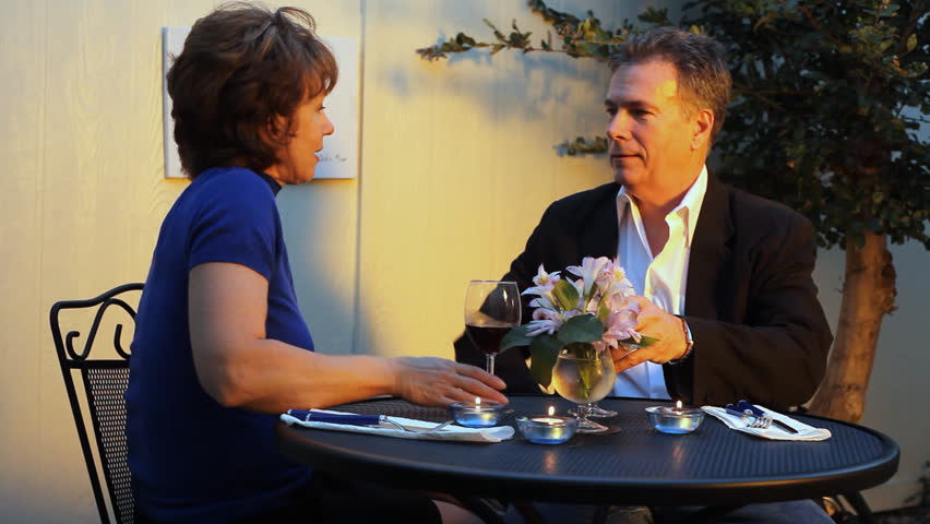 A warm golden glow lights the scene of a mature couple enjoying a glass of wine outside a little cafe