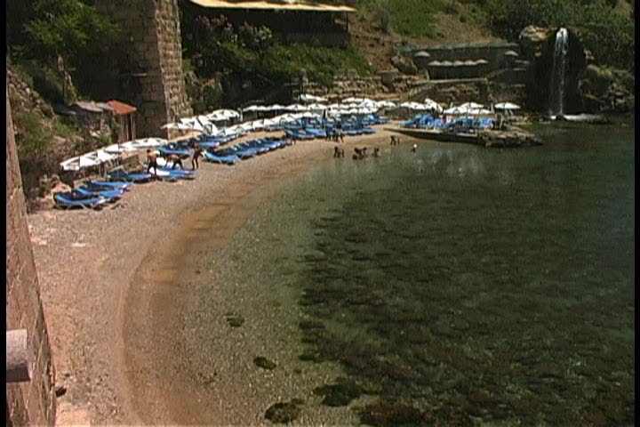 Pan of a rocky cove with a waterfall and fountain