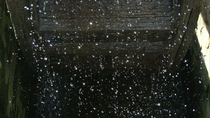 Close-up on falling water drops from rotating mill-wheel.