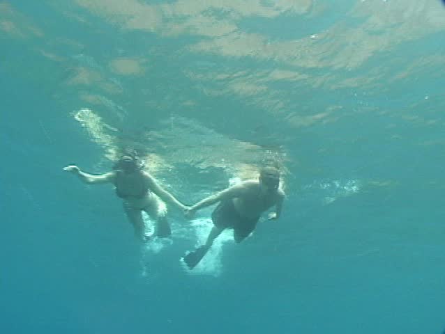 Underwater perspective of couple holding hands as they snorkel overhead.
