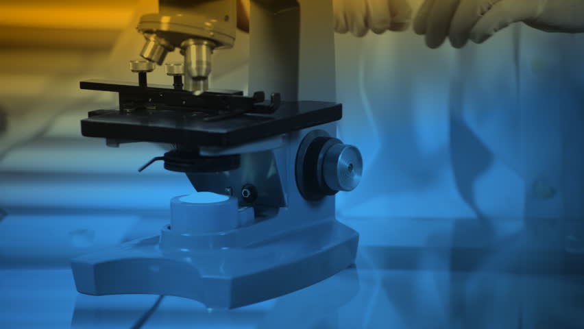A young lab technician examines a specimen he has placed under his microscope. Blue and yellow gel affect applied.
