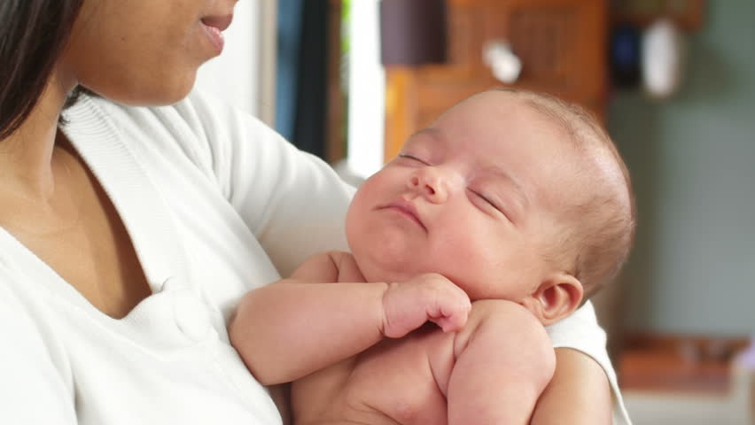 An adorable little newborn baby is sound asleep in her mother's arms. Close up shot.