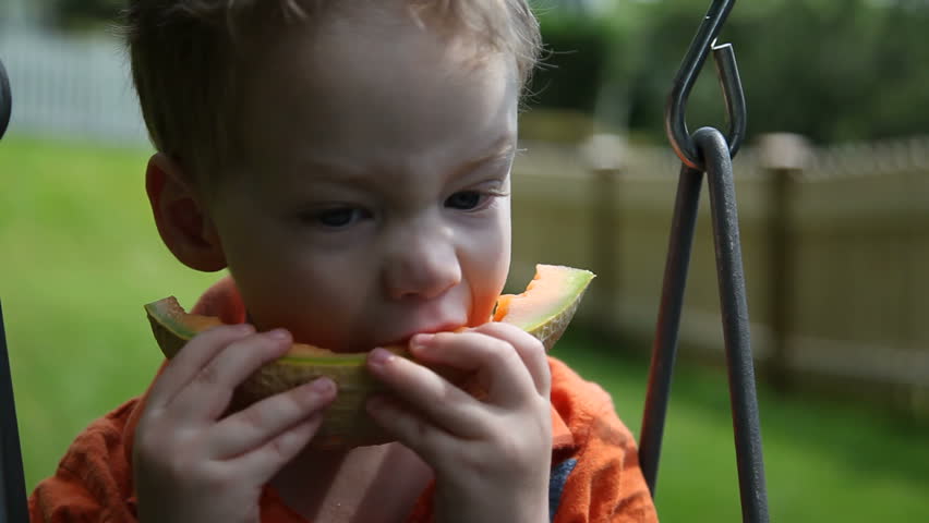 Young boy eating melon on swing