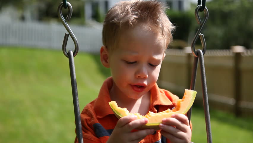 Young boy eating melon on swing
