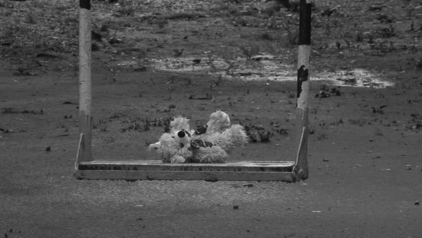 Forgotten Teddy bear on a swing under rain. Deep depression theme. Black and white.