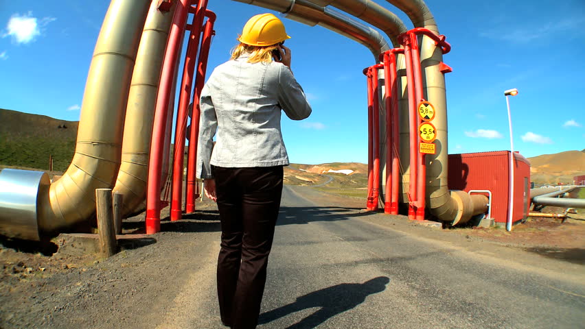 Female geothermal energy technician using a mobile (cell) phone while surveying the power plant