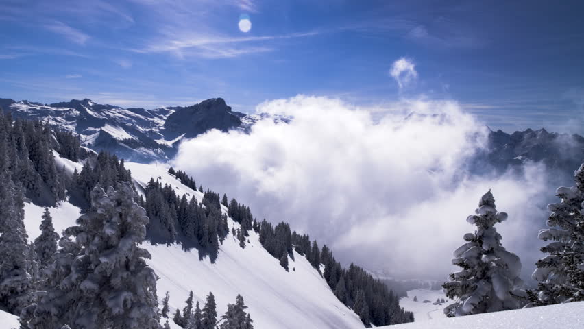 Moving winter postcard: Snowy hills. Dramatic clouds form in a valley. View from the top of a mountain. Time lapse