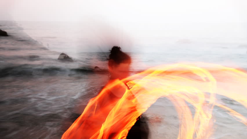 a woman does a fire performance on the beach