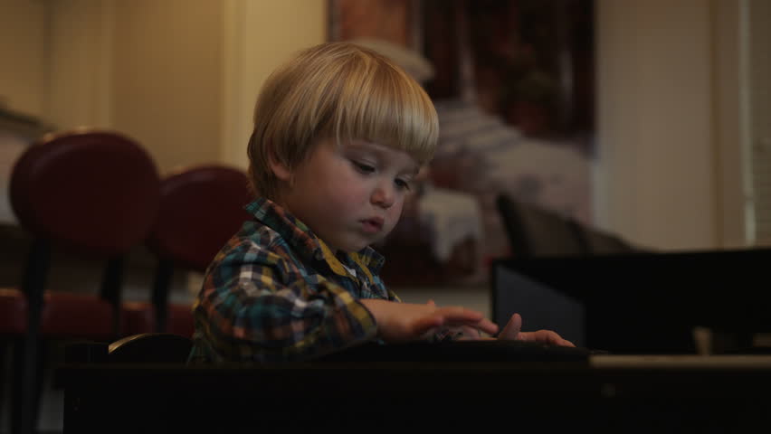 A young boy drags objects around the screen of a tablet while sitting at a small table.
