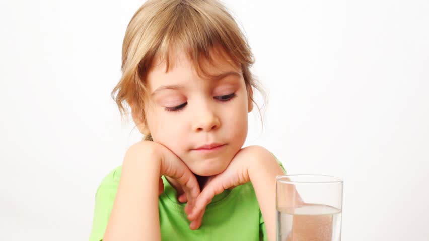 small girl drinks water from glass and smiles on white background 