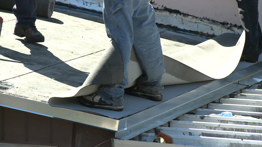 Roofers installing the final layer of membrane using hot bitumen on a flat roof