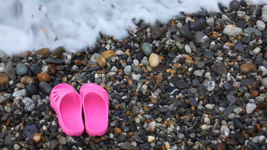 children's pink slippers on pebble beach with sea surf 