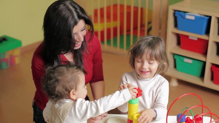 female teacher, toddler and 2-3 year girl playing with blocks toy in kindergarten