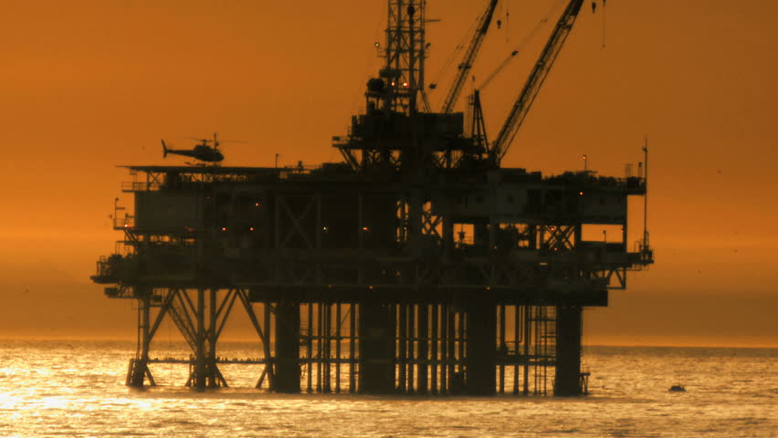 Helicopter taking off at sunset from oil rig at sea 