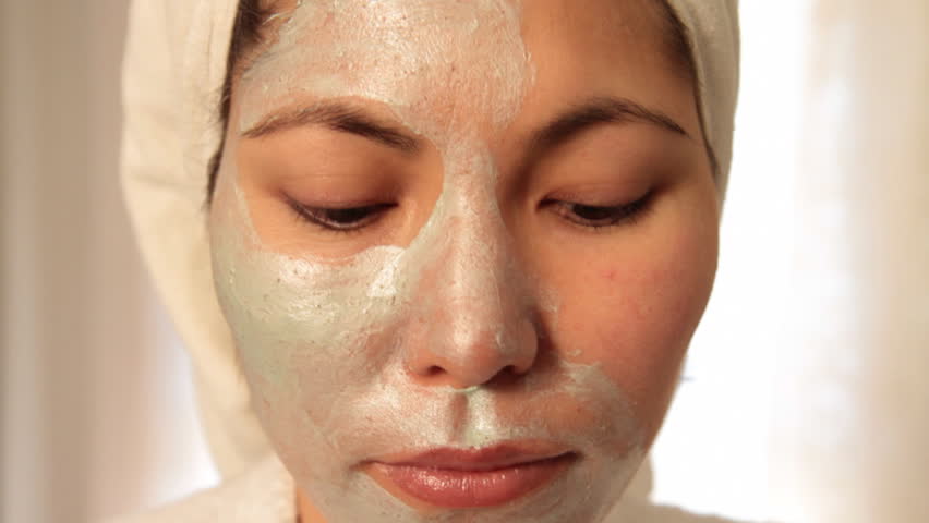 Young Asian woman looks into camera and applies scrub on her face 