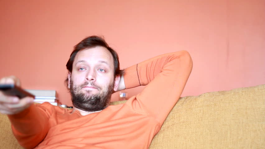 Dolly shot of a bored Man changing channels on tv with remote control - 1080p