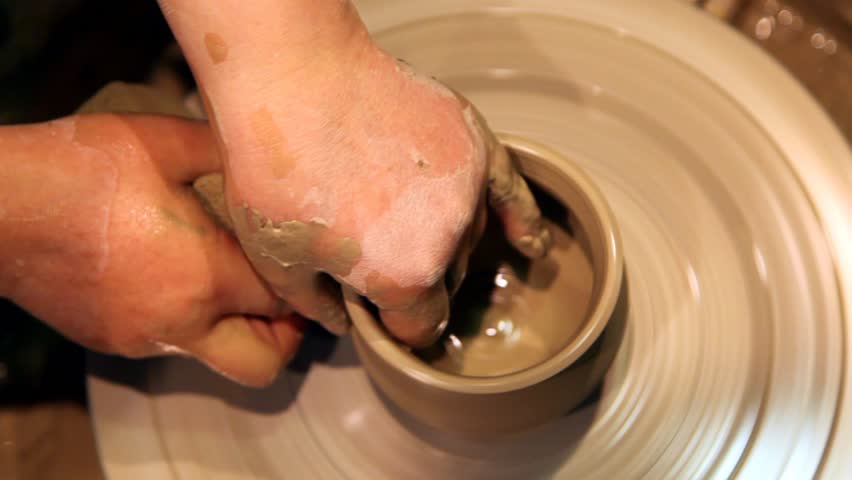 top view close up as pair of hands forms clay pot on potter's wheel 