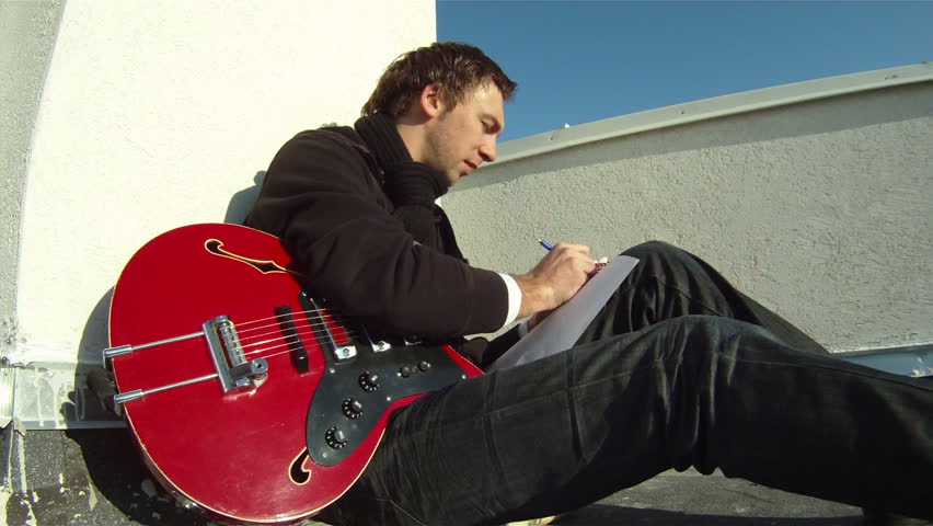 The musician is working on the roof. The musician sits on the roof playing the guitar and writes songs.