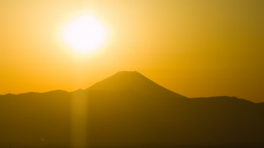 Time-lapse sun in orange sky sinking behind a city on a bay