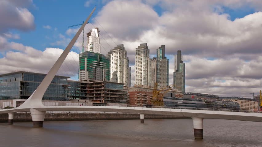 Puente de la Mujer, a modern footbridge and landmark of Buenos Aires, Arg, in front of office buildings. Photo time-lapse with sunlight "flashing" through dark clouds (C. 40D, DSLR). 