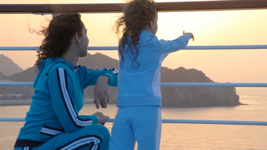 a mother and her little daughter watch the sun set from a ship