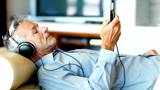 Relaxed senior man listening to music with headphone while lying on sofa at home