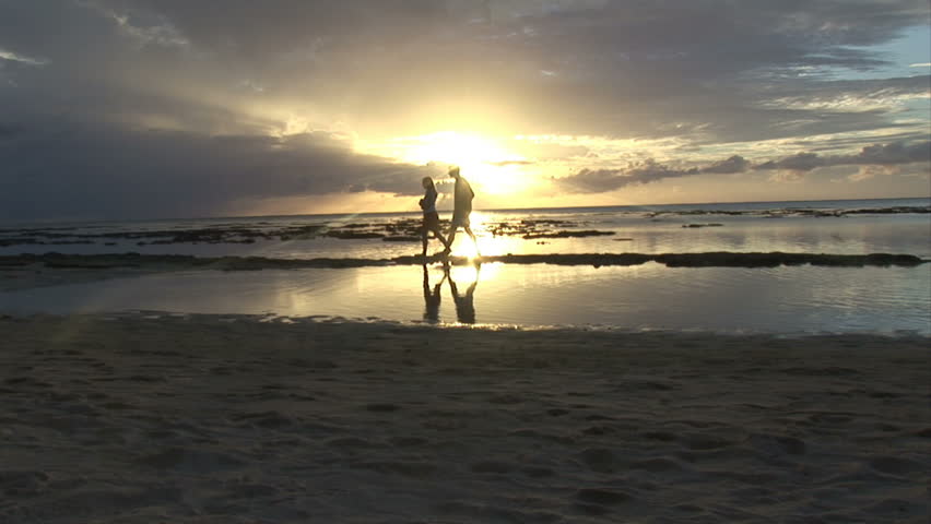 A couple walk hand in hand along a tropical and peaceful shoreline