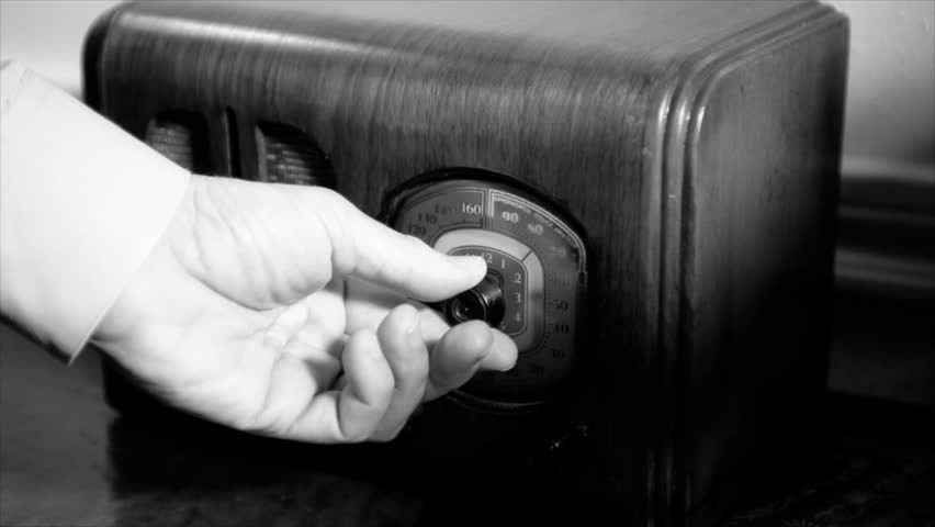 A man's hand turns the dial on an old vintage 1940's radio until he finds the music he is looking for, stops and starts tapping his finger. Film Noir
