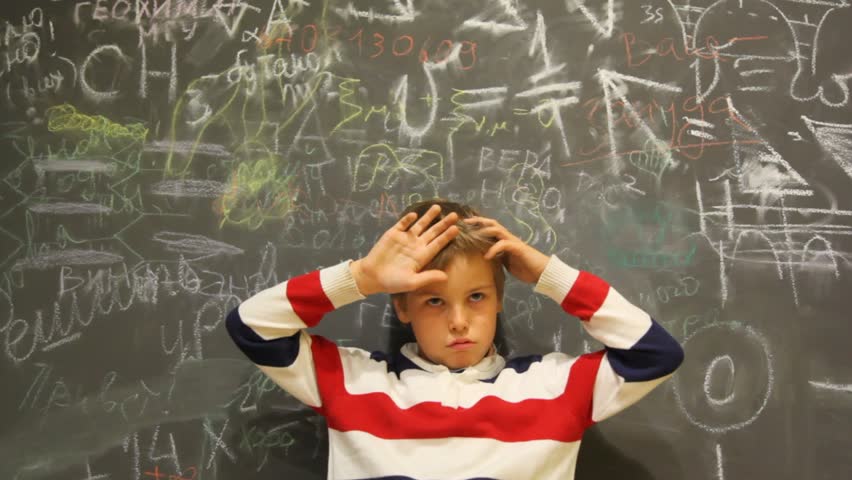 puzzled boy stands against chalkboard covered with writing