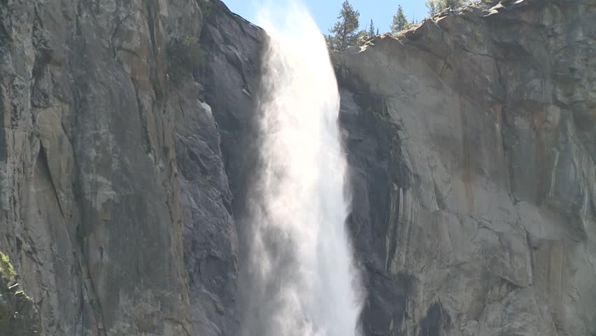 The swirling mist in the morning sun belies the torrent of water pouring over Yosemite's Bridalveil Falls in June 2010.  Med shot of falls zooms to wide shot.  :59