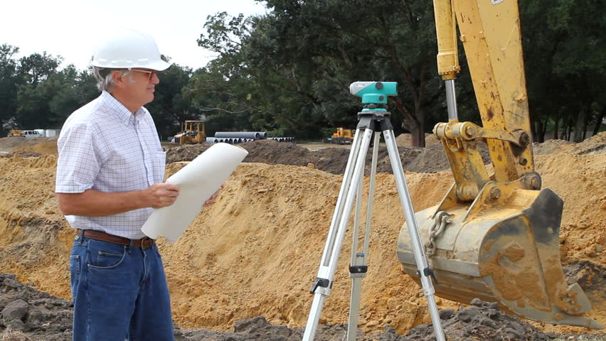 Civil engineer reads architectural blueprints and inspects the work at a construction site.