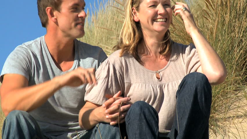 Attractive young caucasian couple enjoying quiet time together sitting in sand dunes at the coast filmed at 60FPS