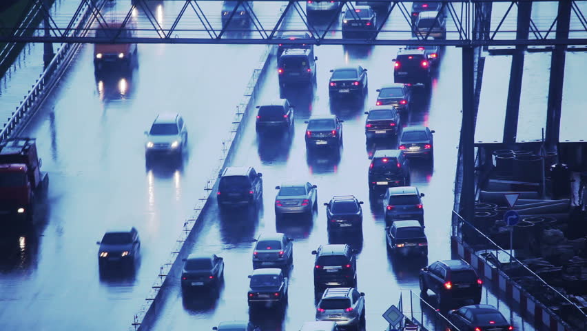Many cars moving on freeway in traffic jam on a rainy day at twilight.