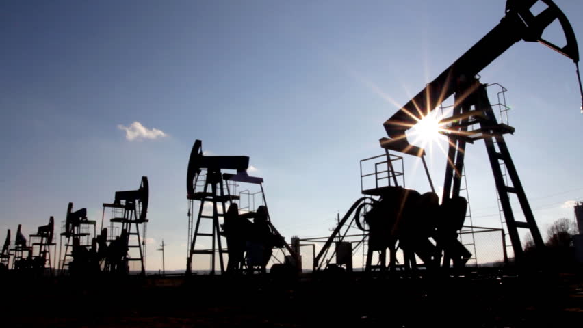working oil pumps silhouette against sun