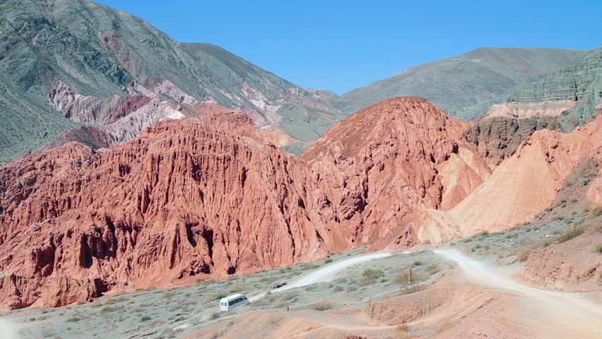 Colorful mountain landscape of the Quebrada de Humahuaca valley. Tourist busses ascend a road of a scenic circuit (Purmamarca, Jujuy pr., Argentina; 1080p, C. 7D).