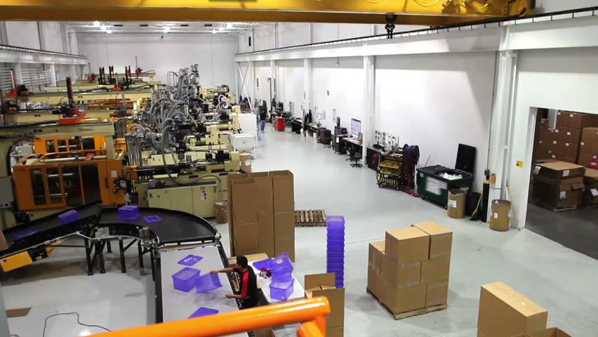 The camera pans across a large assembly factory and ends on a supervisor looking at his clipboard. 