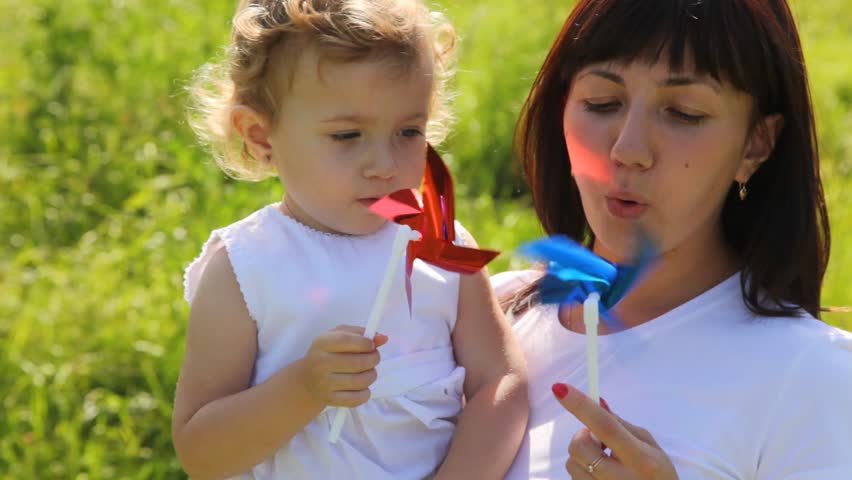 mother and daughter are blowing on the windmill sunny and warm summer day