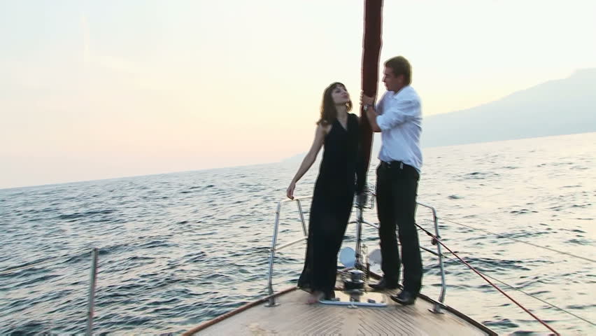 A beautiful young couple standing on the edge of the boat during a strong pitching. 