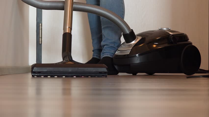 A Woman Vacuums A Hall In An Apartment Closeup From The Floor