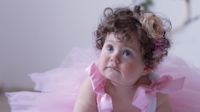 Unhappy Little Girl With Curly Hair In A Pink Dress Close Up Posing In