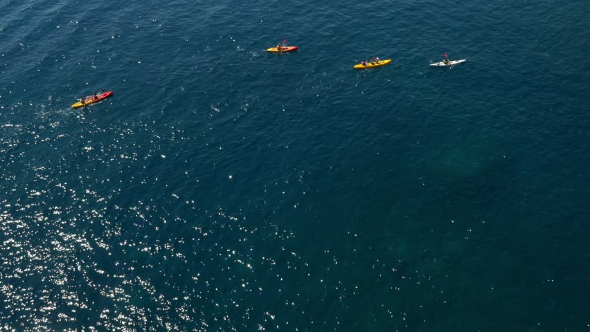 Long shot aerial shot of a large group of sea kayakers following their leader in the open sea