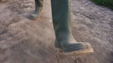 Farmer walking on dusty dirt country road in sunset, close up of rubber boots, low angle view