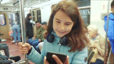 Teenage girl with smartphone and headphones inside a subway car a lot of  people crowd underground subway. metro underground people concept. young  girl brunette daughter search the internet on the web