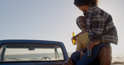 African american woman on mans lap sitting on a pickup truck at beach. They are drinking beer