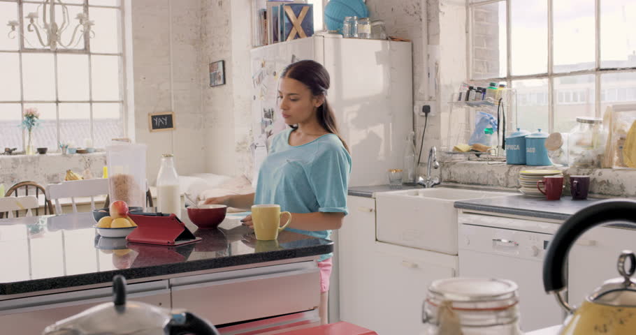 Pretty Hispanic At Kitchen Counter Amidst Breakfast Cereal And Pretty Hispanic At Kitchen Counter Amidst Breakfast Cereal And Milk Using Digital Tablet Touch Screen