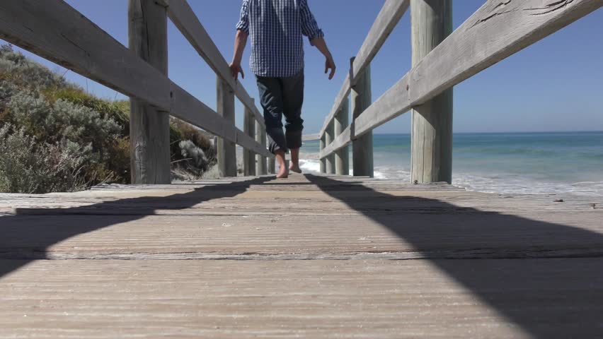 Ground Level View Of Man Walking Barefoot Down Timber Boardwalk Up On