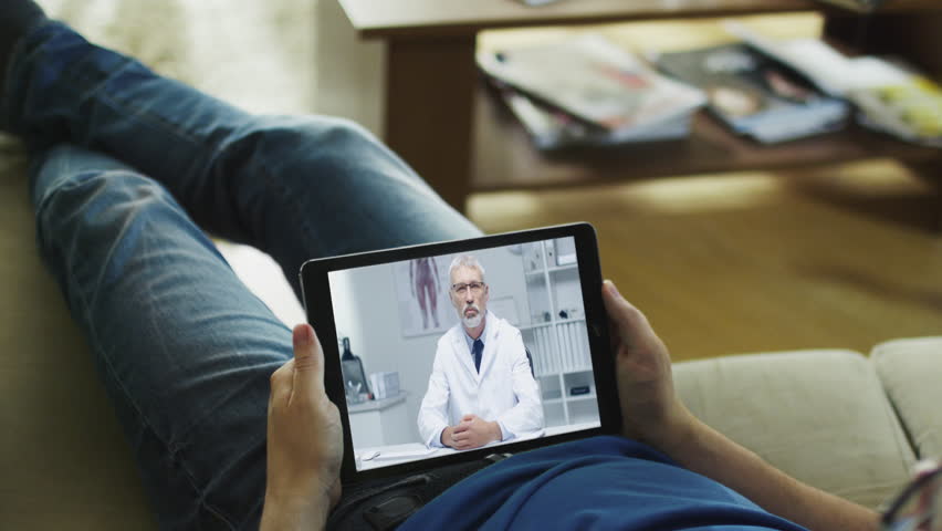 Sick Man Lying on a Couch and Having Video Conversation with His Doctor on a Tablet Computer.
