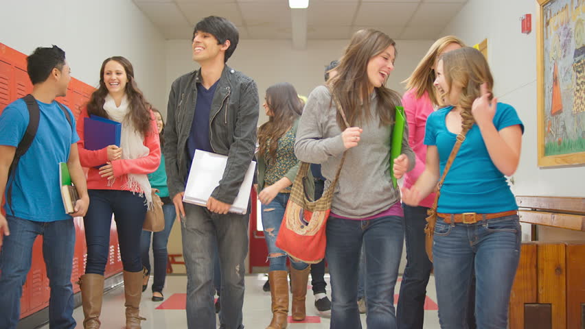 A group of students walk up the stairs and down the hallway towards the camera in slow motion